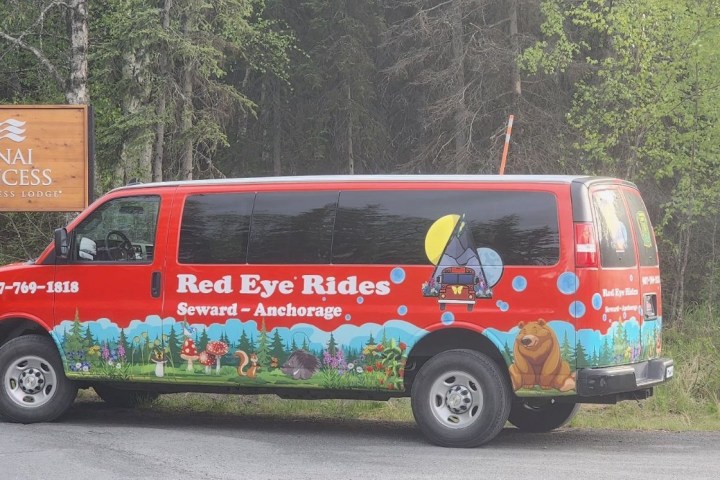 Red van with nature graphics parked near a Kenai Princess sign in a forested area.