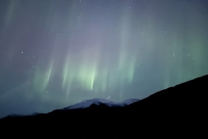 Northern lights with mountain silhouettes beneath a starry sky.