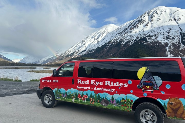 Red van with mountain scenery, snow-topped peaks, and a faint rainbow in the sky.