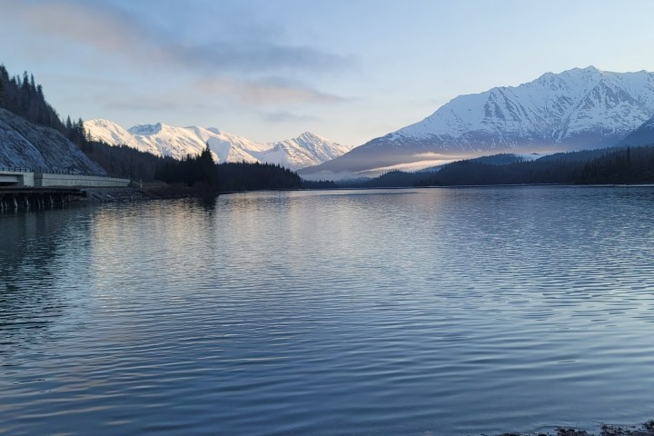 Mountain landscape with snow-capped peaks and a calm lake at dusk.