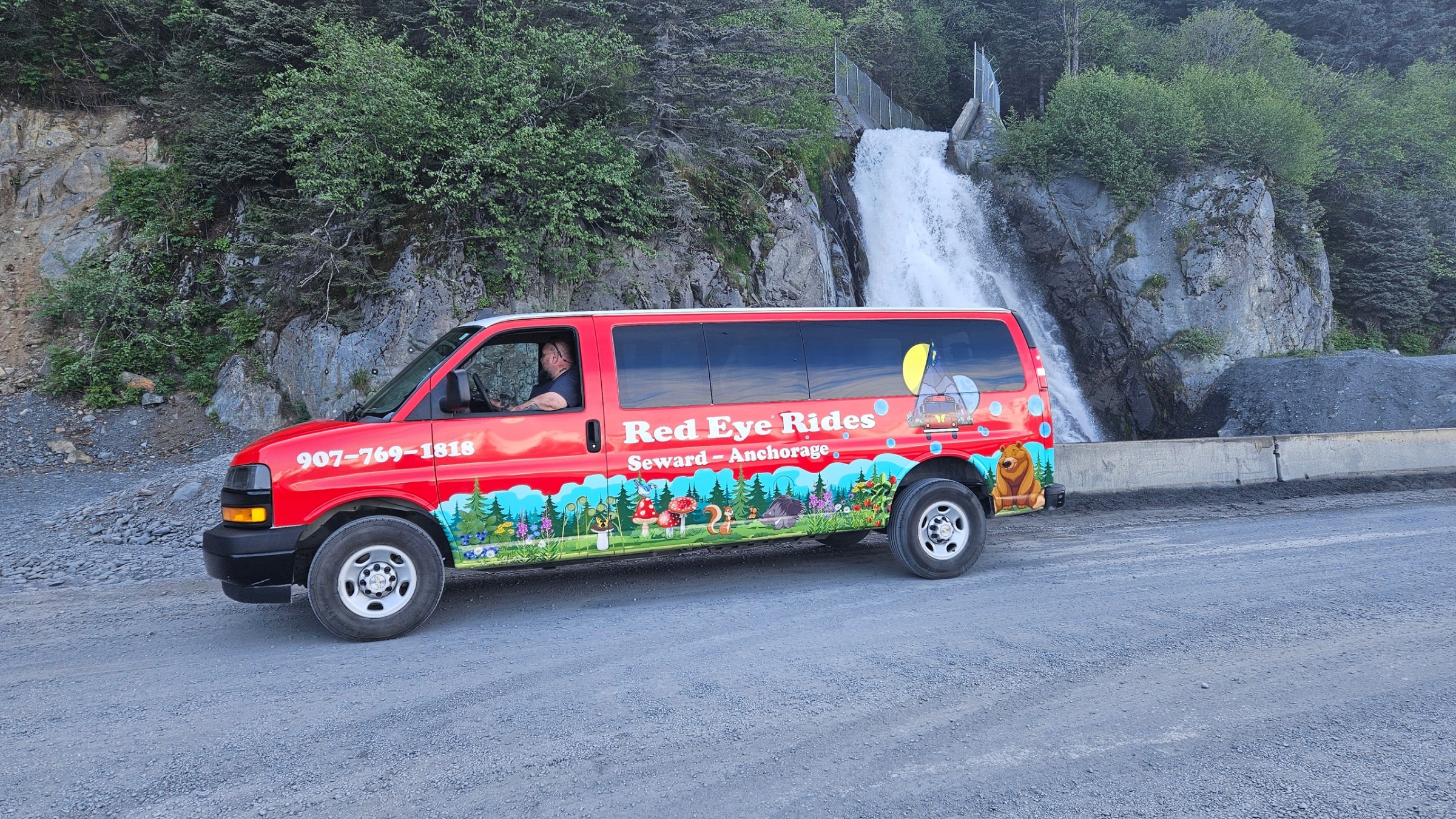Red van with colorful design parked near a waterfall and trees.
