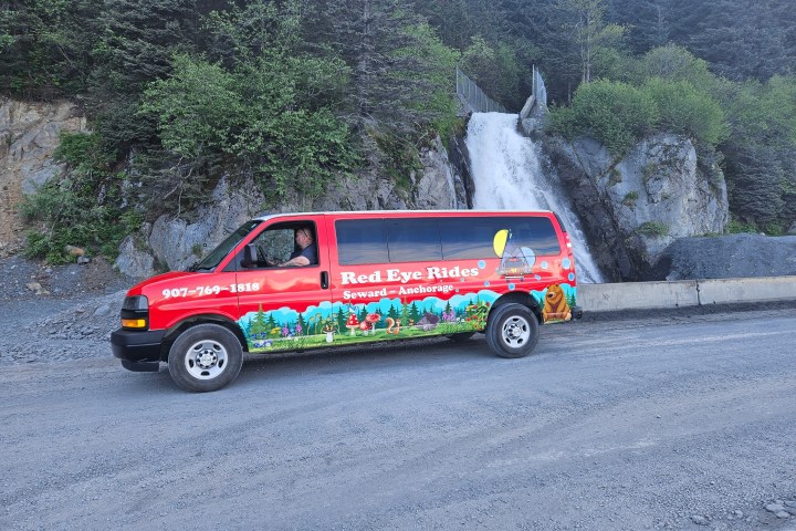 Red van with colorful design parked near a waterfall and trees.