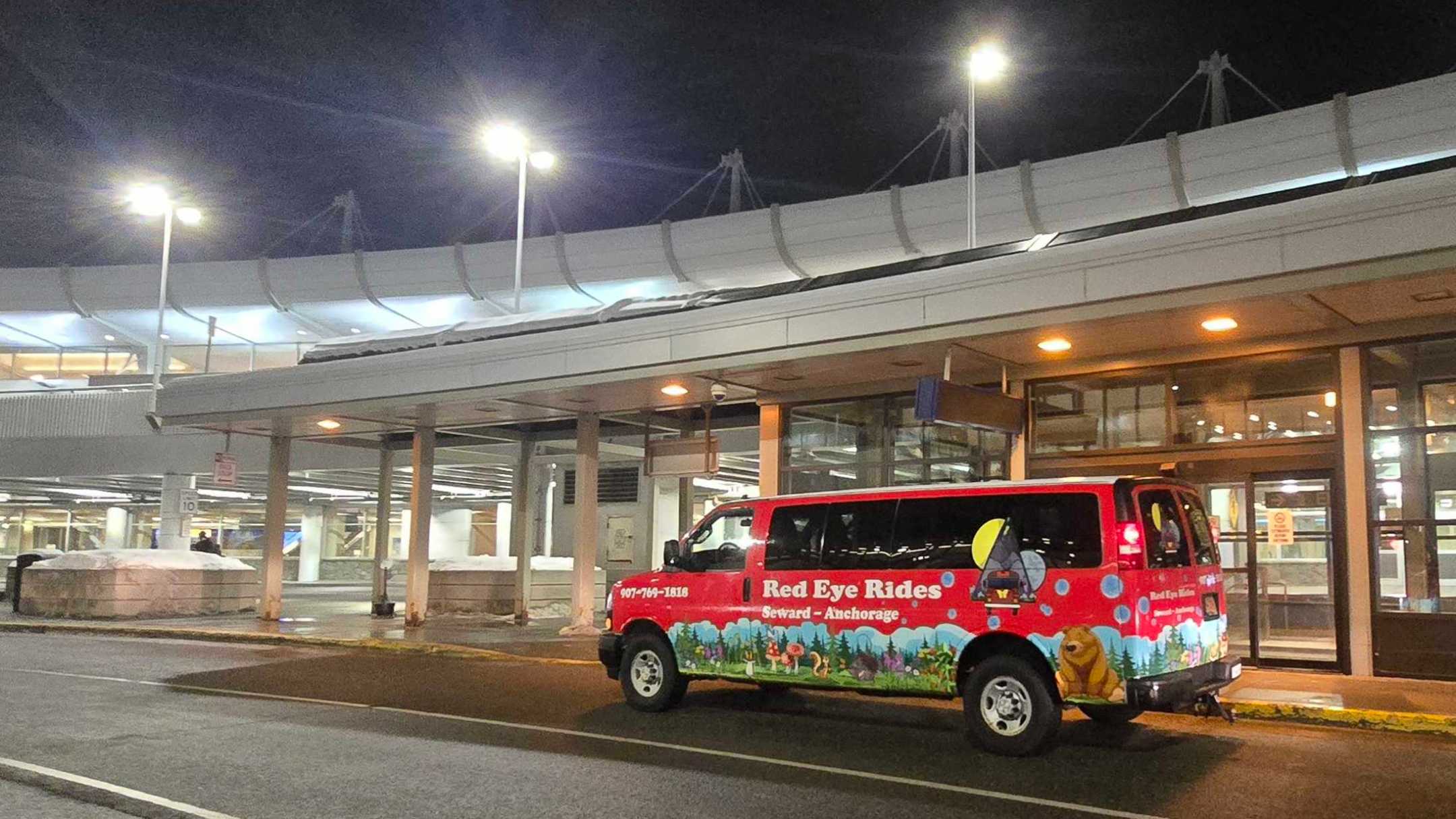 Red van parked outside a brightly lit building at night.