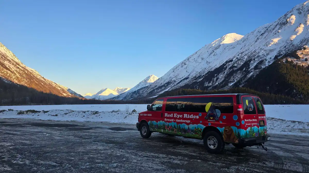 Red van parked on snowy road with mountains in the background.
