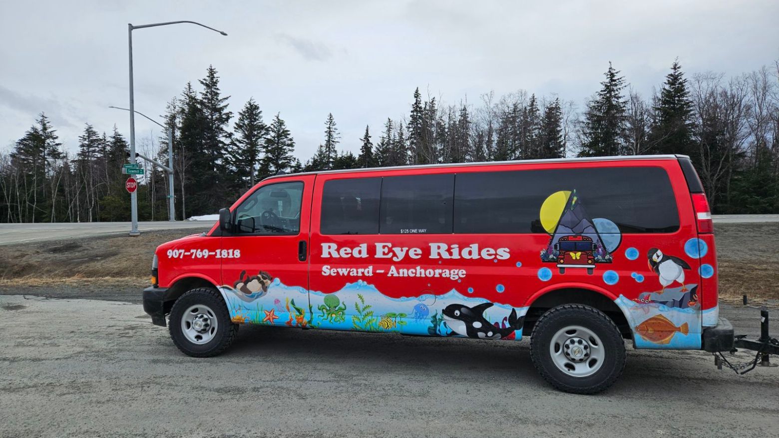 Red van with 'Red Eye Rides' and sea-themed graphics, parked on roadside.